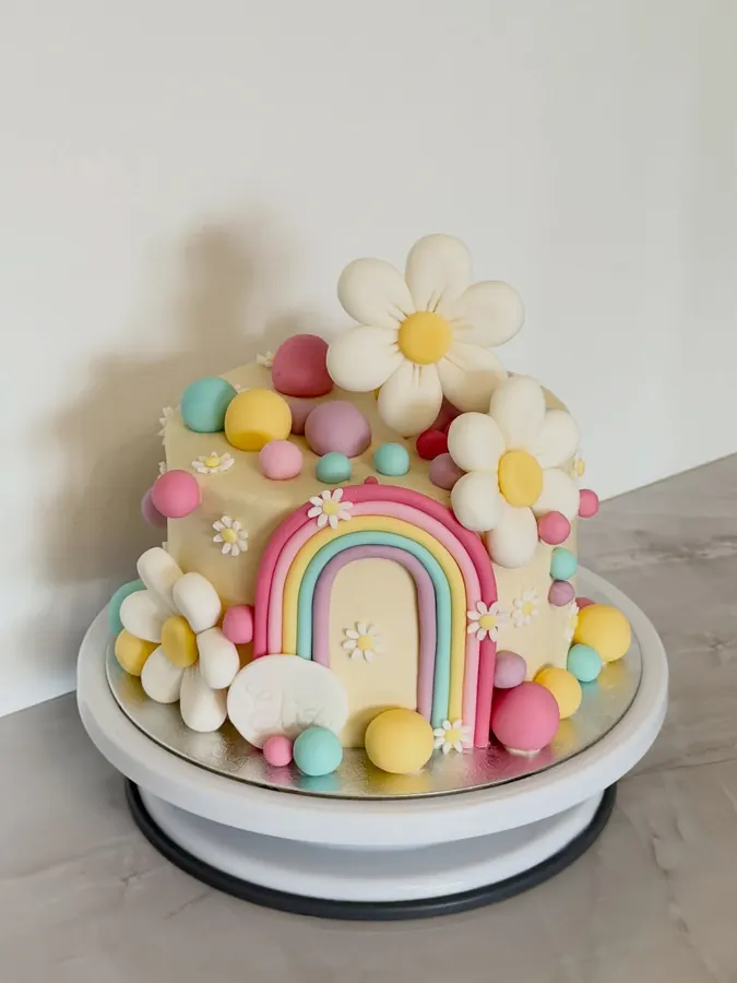 Torte mit modelliertem Regenbogen, Gänseblümchen und bunten Kugeln