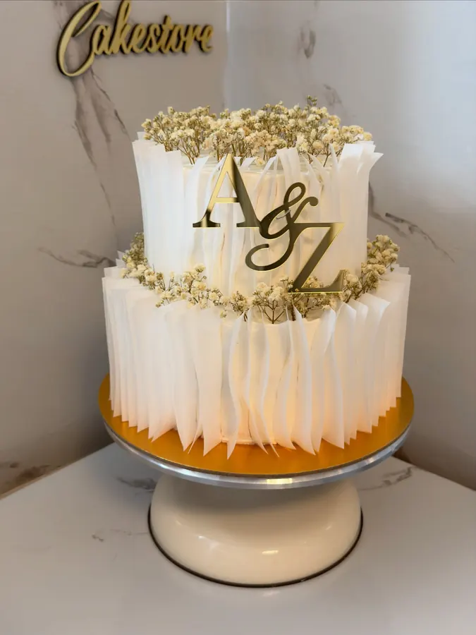 Zweistöckige Torte mit weißen Rüschen, Schleierkraut und goldenem Monogramm