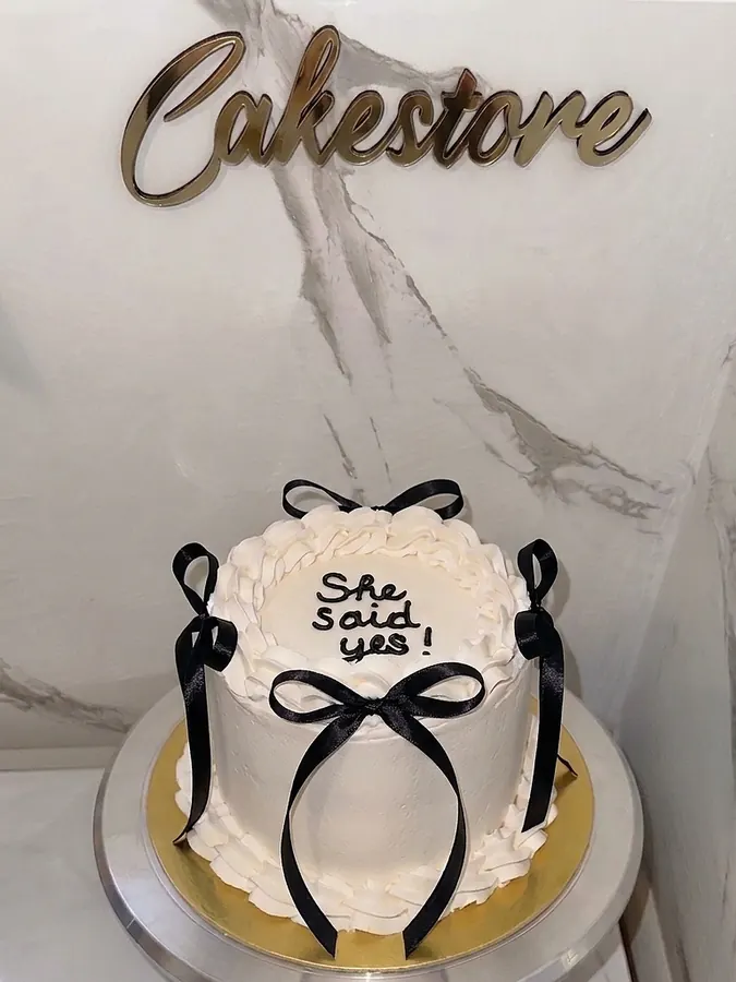 Kleine Cremetorte mit schwarzen Schleifen und verspielter Aufschrift